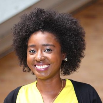 Close-up photograph of a Black woman with an afro, smiling widely.