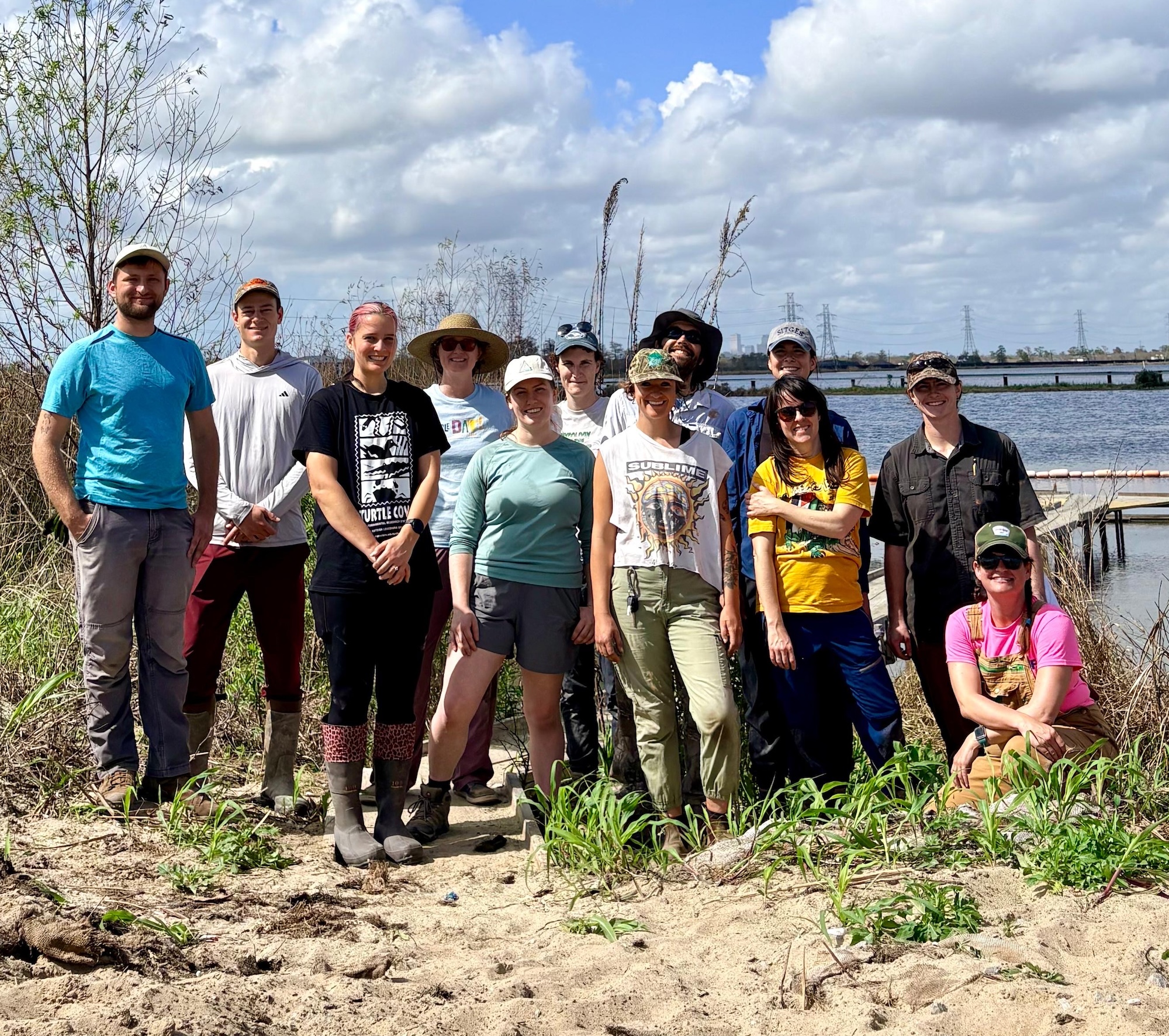 Group of people standing in a grassy area by a body of water.