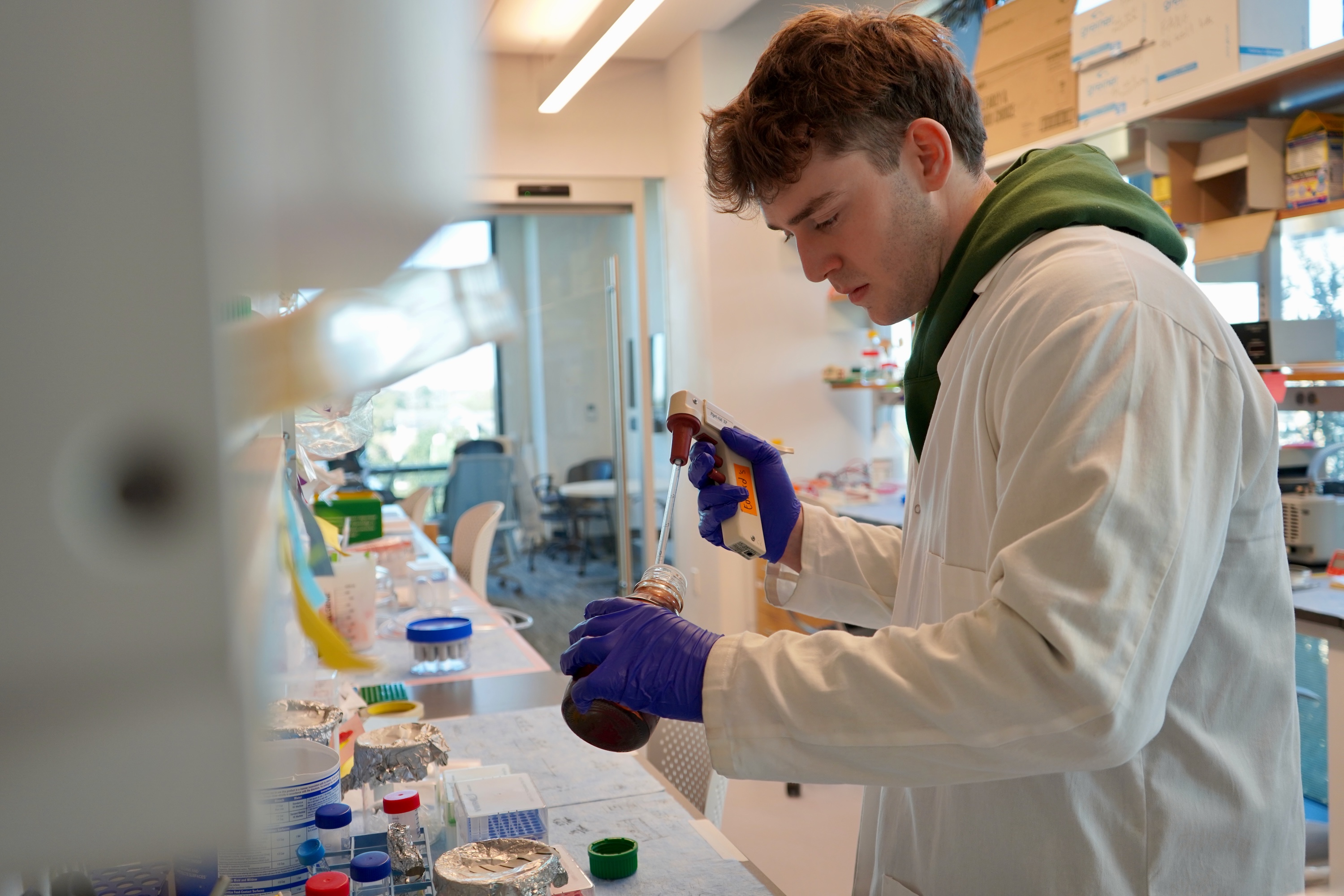 Young man in lab coat and gloves works with liquids in a laboratory.