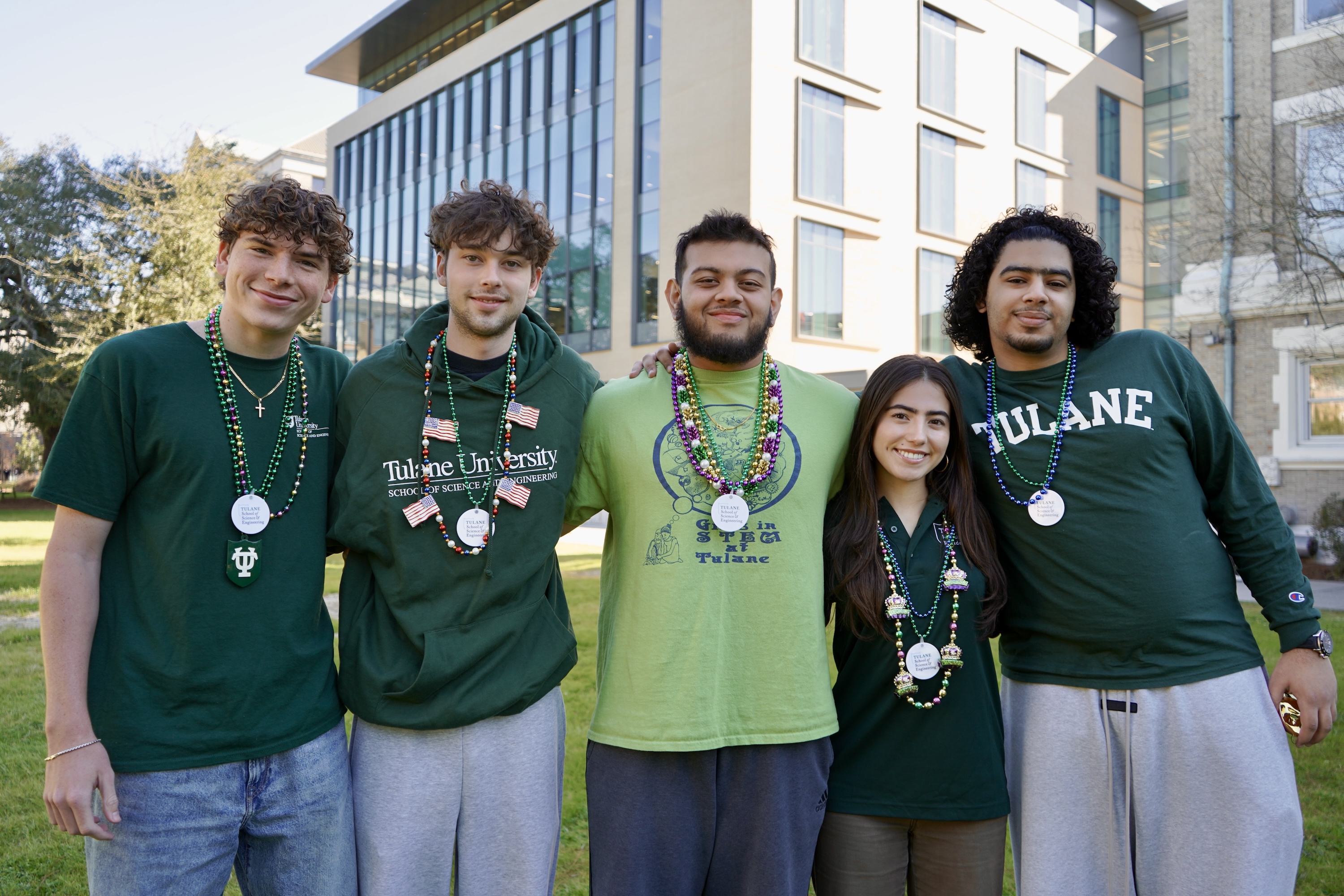 Five young adults in green sweatshirts pose outdoors with medals.