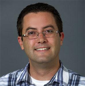 Man with glasses wearing a blue plaid shirt, smiling.