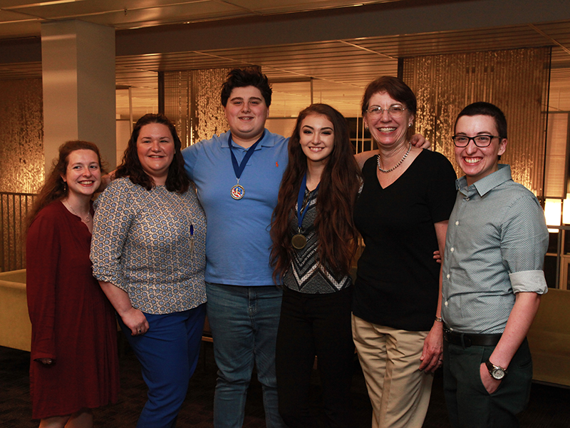 Six smiling people, four younger and two older, posing for a photograph.