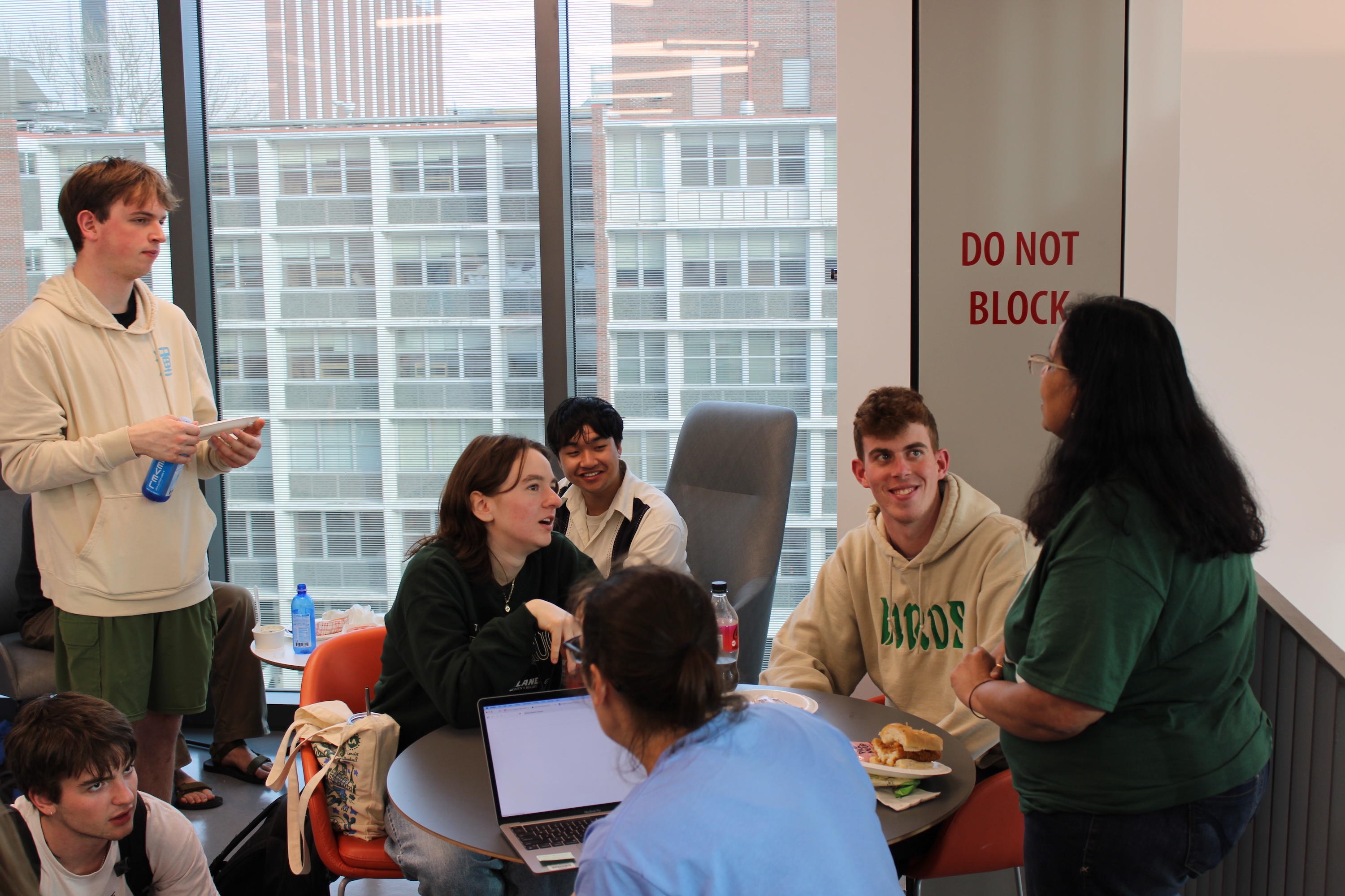 A group of students in a lounge area, some talking, others looking at a laptop.