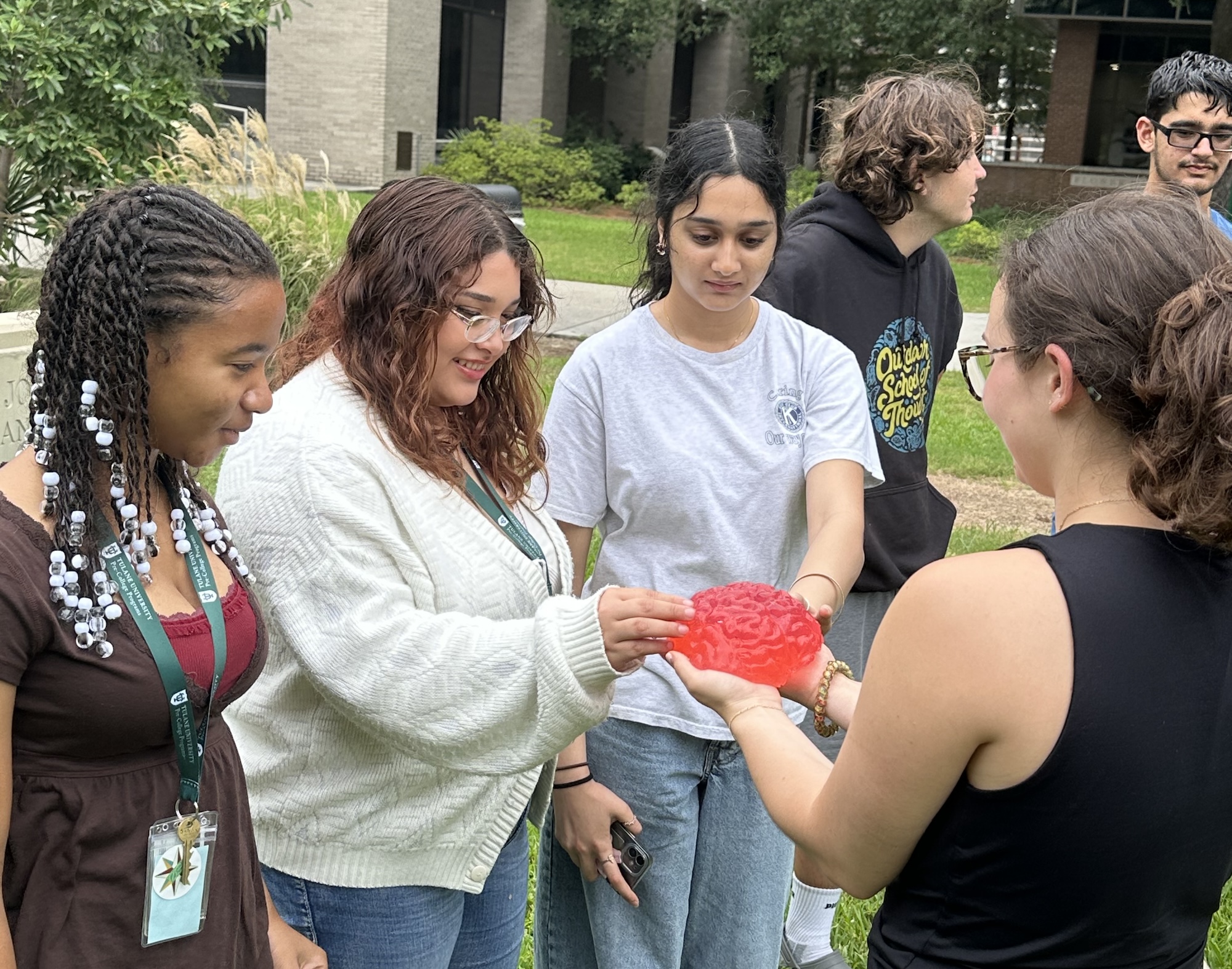 Four young adults observe a translucent, red, brain-shaped object held by one of them.