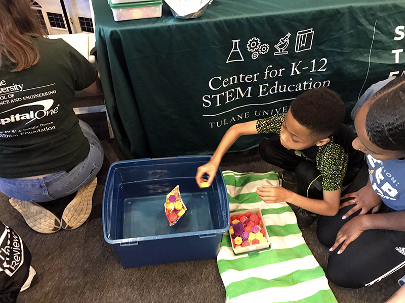 Boy plays with a paper boat in water at a STEM Education event.