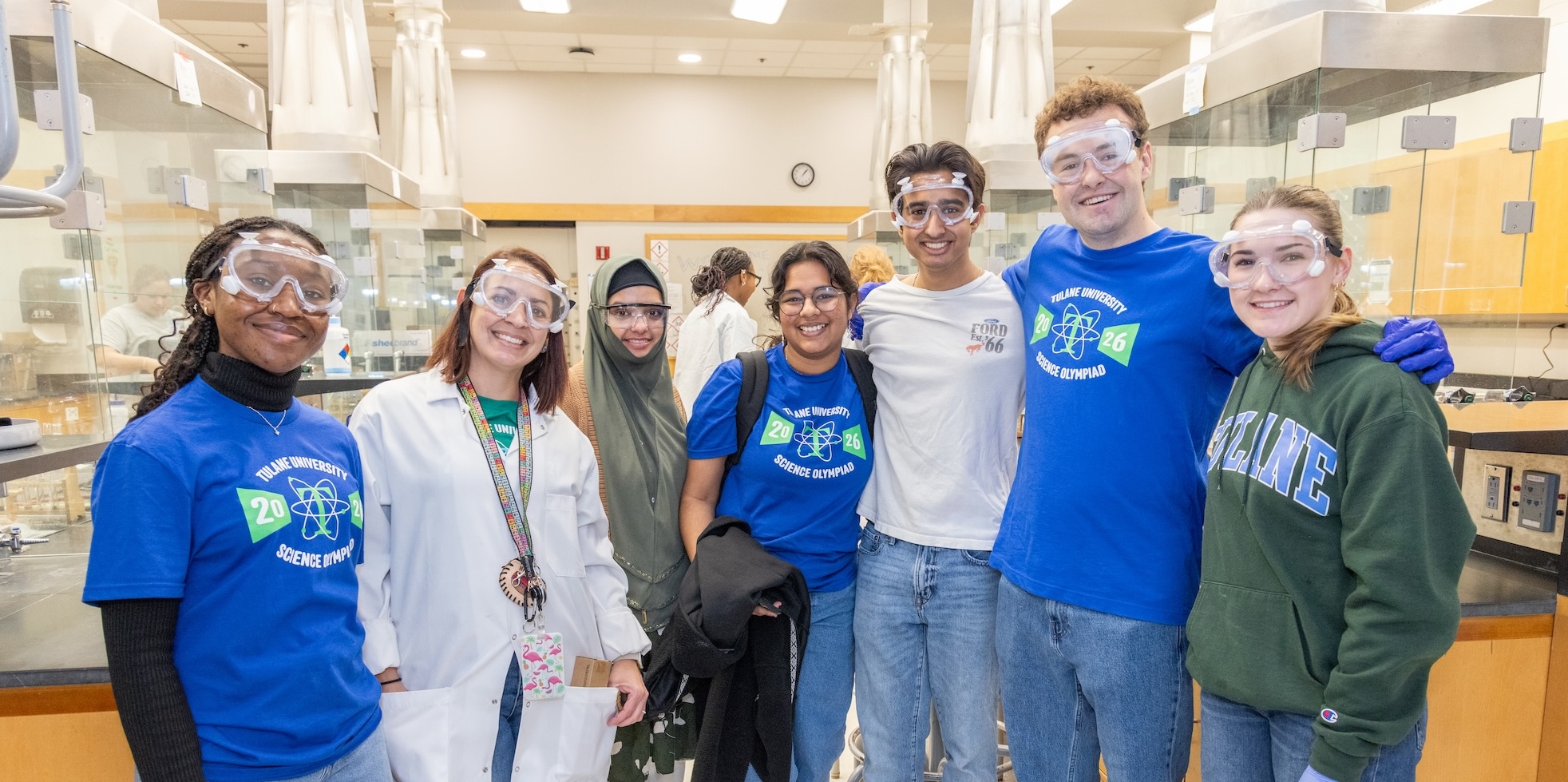Group of six students in a science lab, all wearing safety goggles.