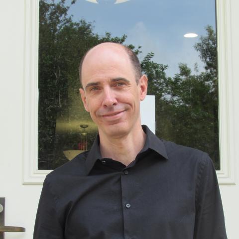 Bald man with a slight smile, wearing a black collared shirt.