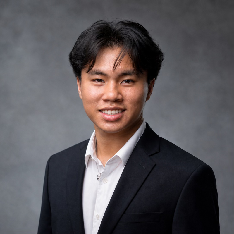 Photograph of a young Asian man in a dark suit smiling against a grey background.
