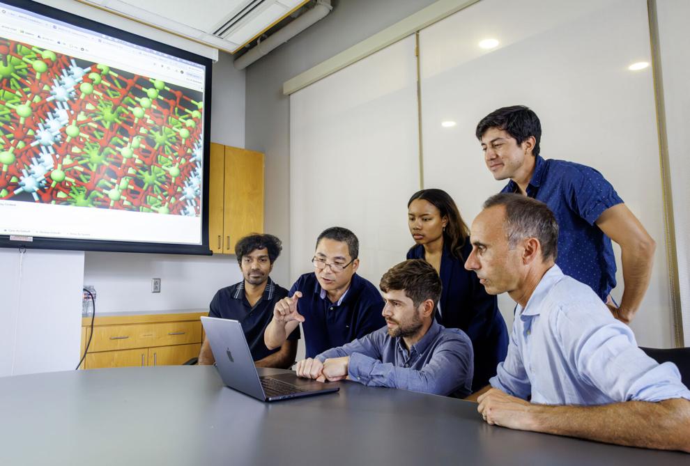 Photo of five colleagues gathered around a laptop in a conference room.