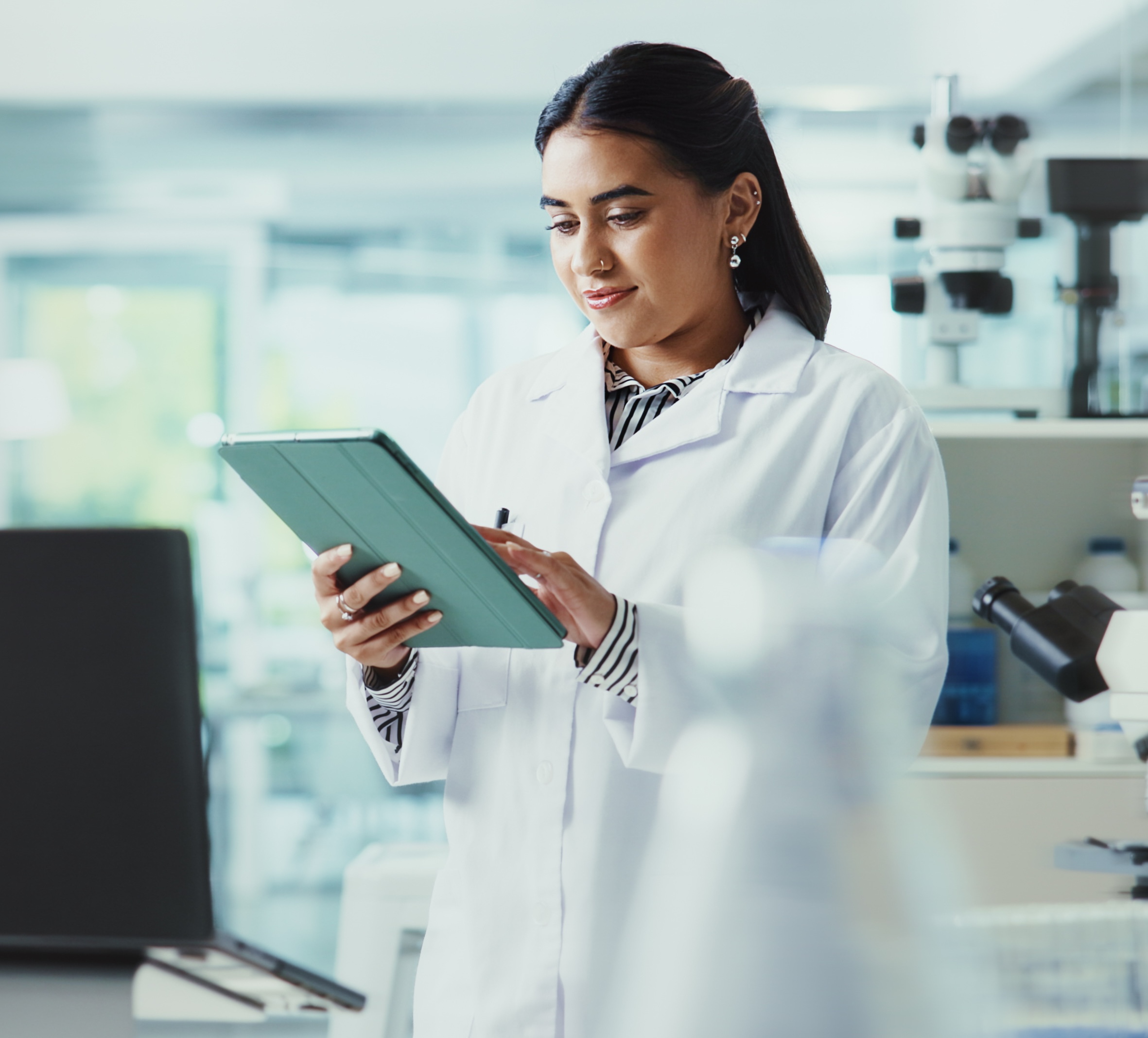 Woman in lab coat uses tablet in bright laboratory.