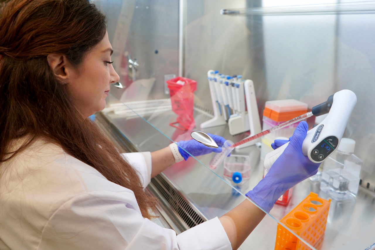 Scientist in lab coat and gloves using a pipette in a biosafety cabinet.