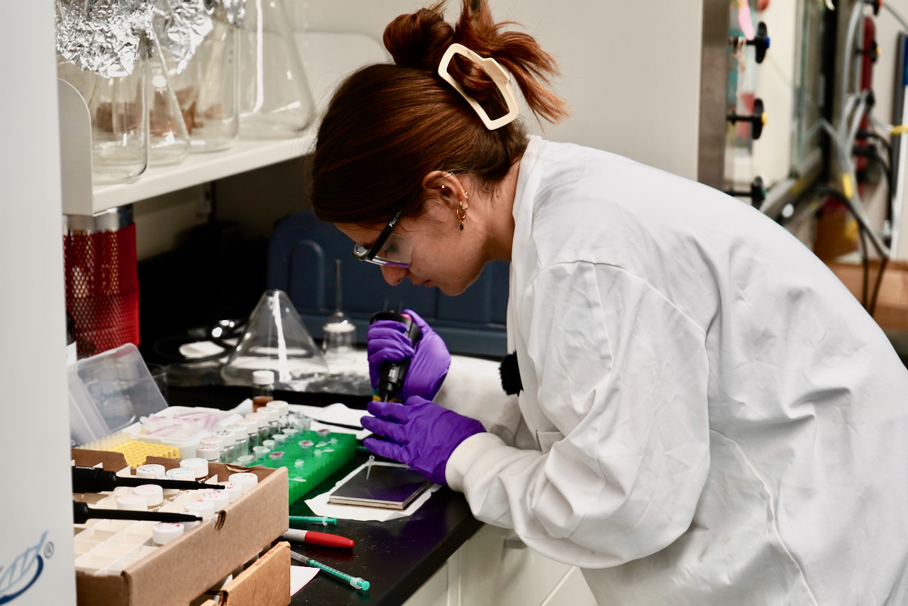 Photograph of a researcher in a white lab coat using a pipette.