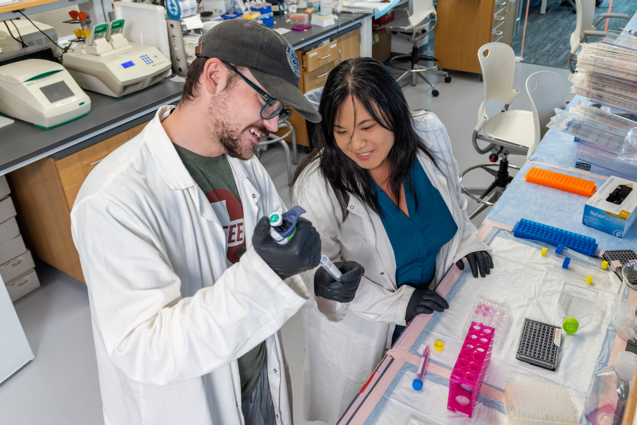 Two people in a lab using a pipette