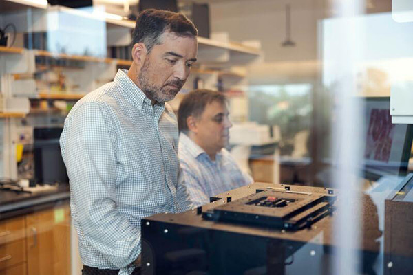 Two men in a lab, one looking at equipment.