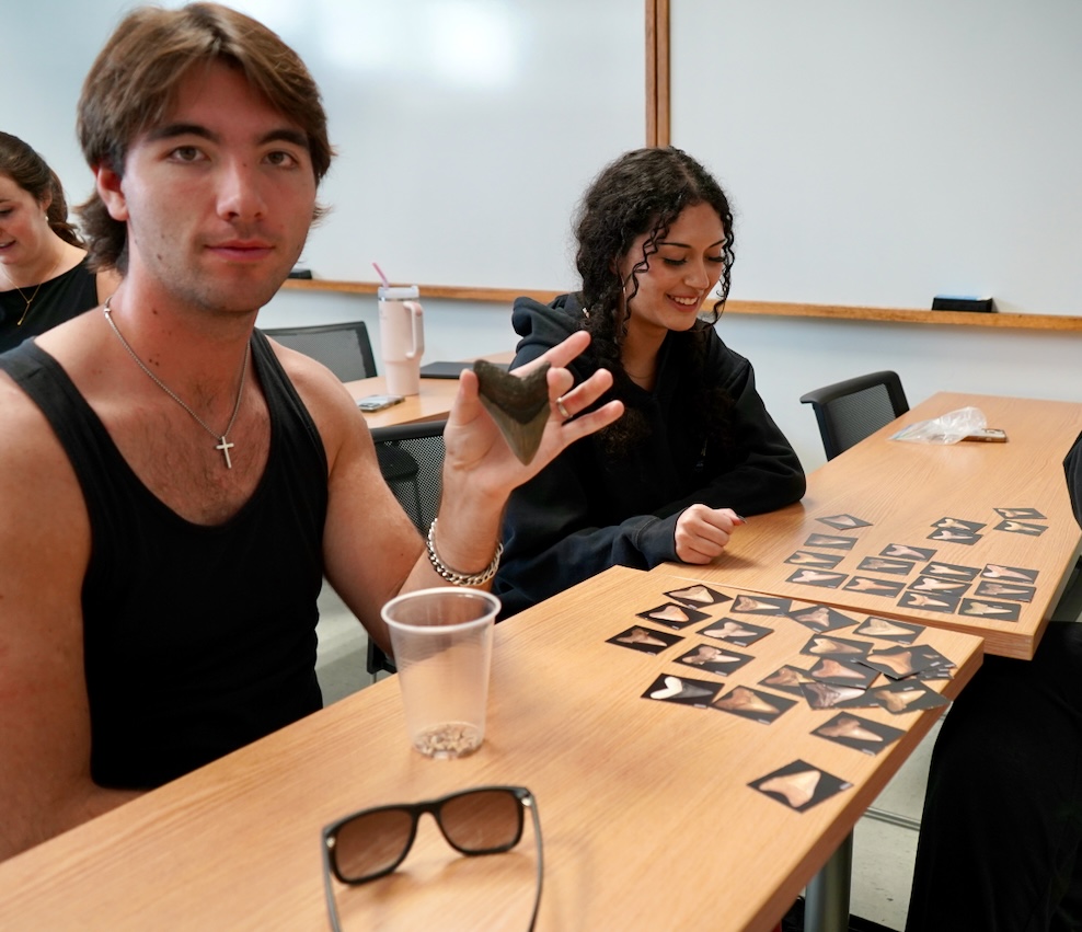 Photograph of students in a classroom, with a young man holding up a fossil.