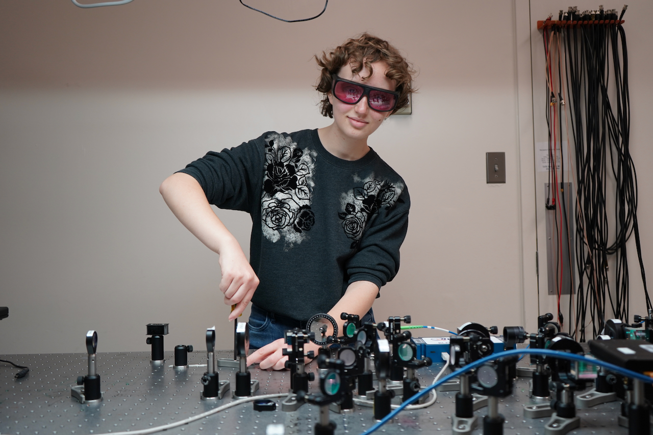 Photograph of a student in safety glasses working on an optical table.