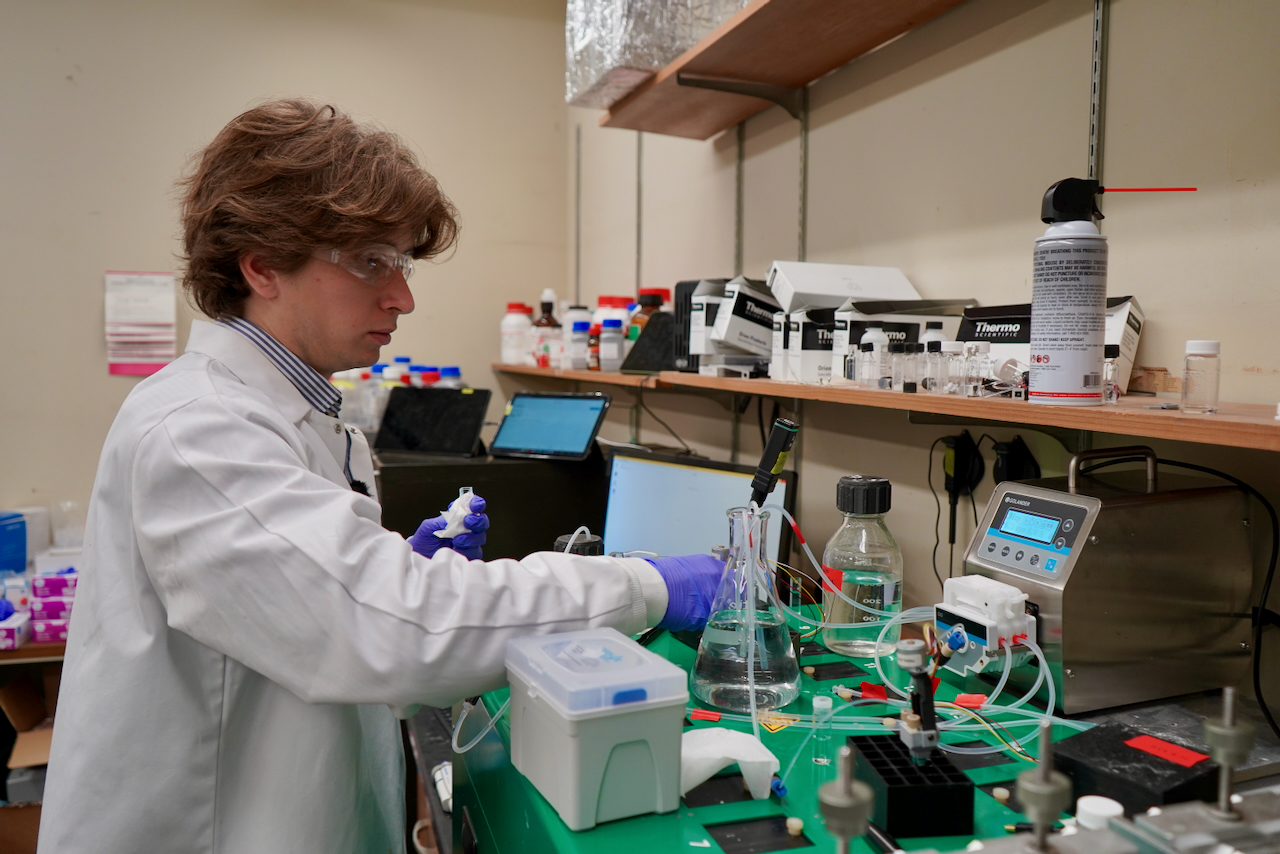 Young scientist in lab coat and goggles works with equipment.