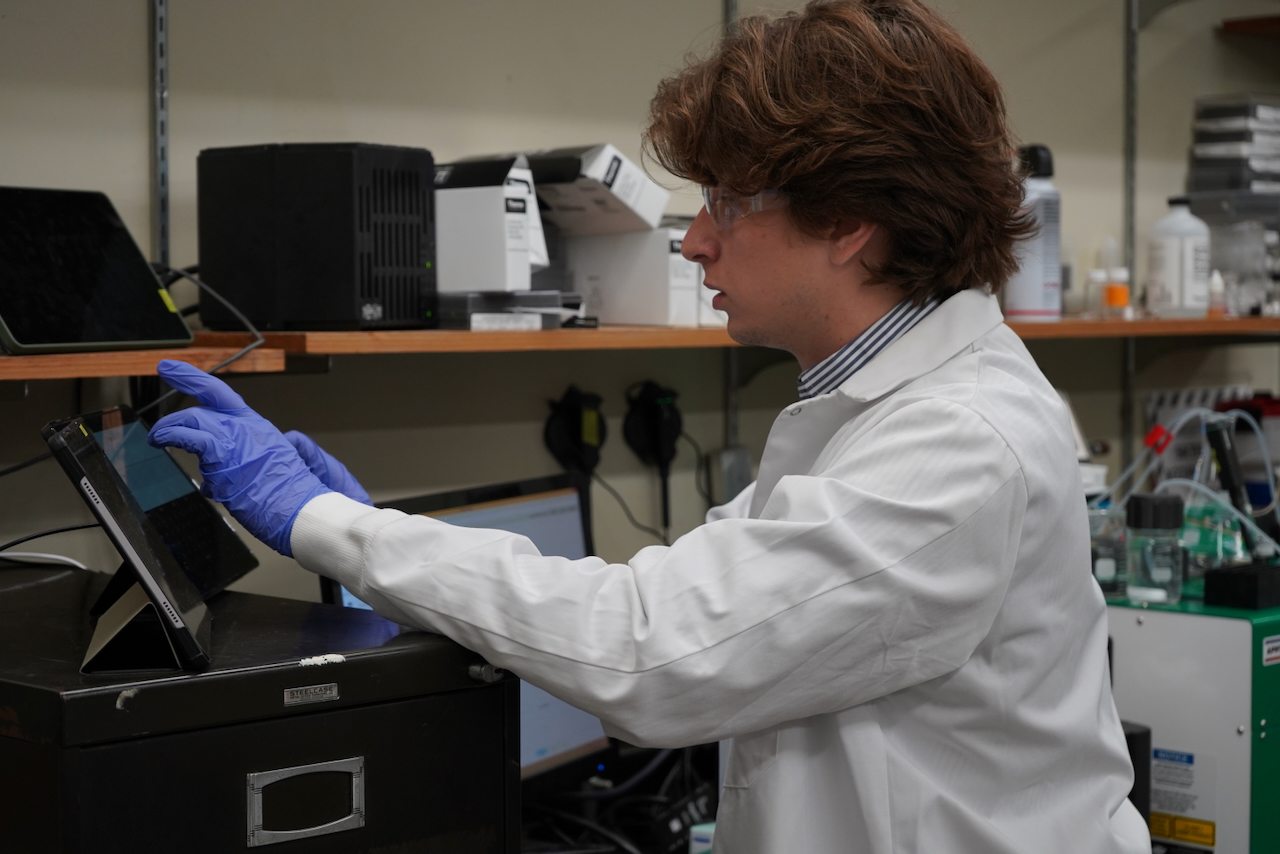 Boy in white lab coat and purple gloves operating lab equipment