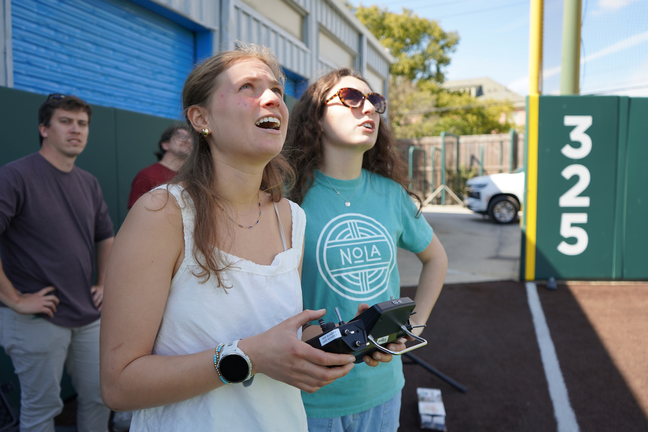 Photograph of people outdoors looking up, holding a drone remote.