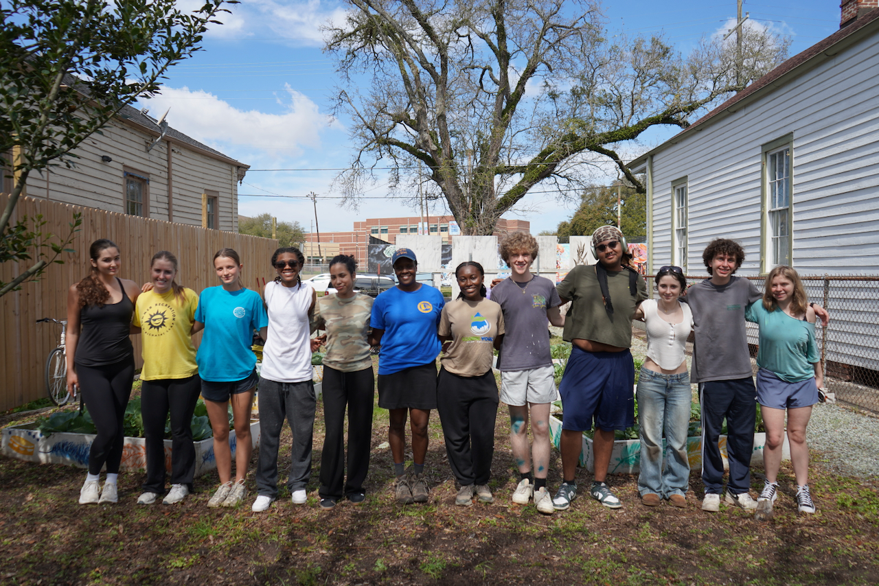 A diverse group of eleven young people stand in a sunny garden.