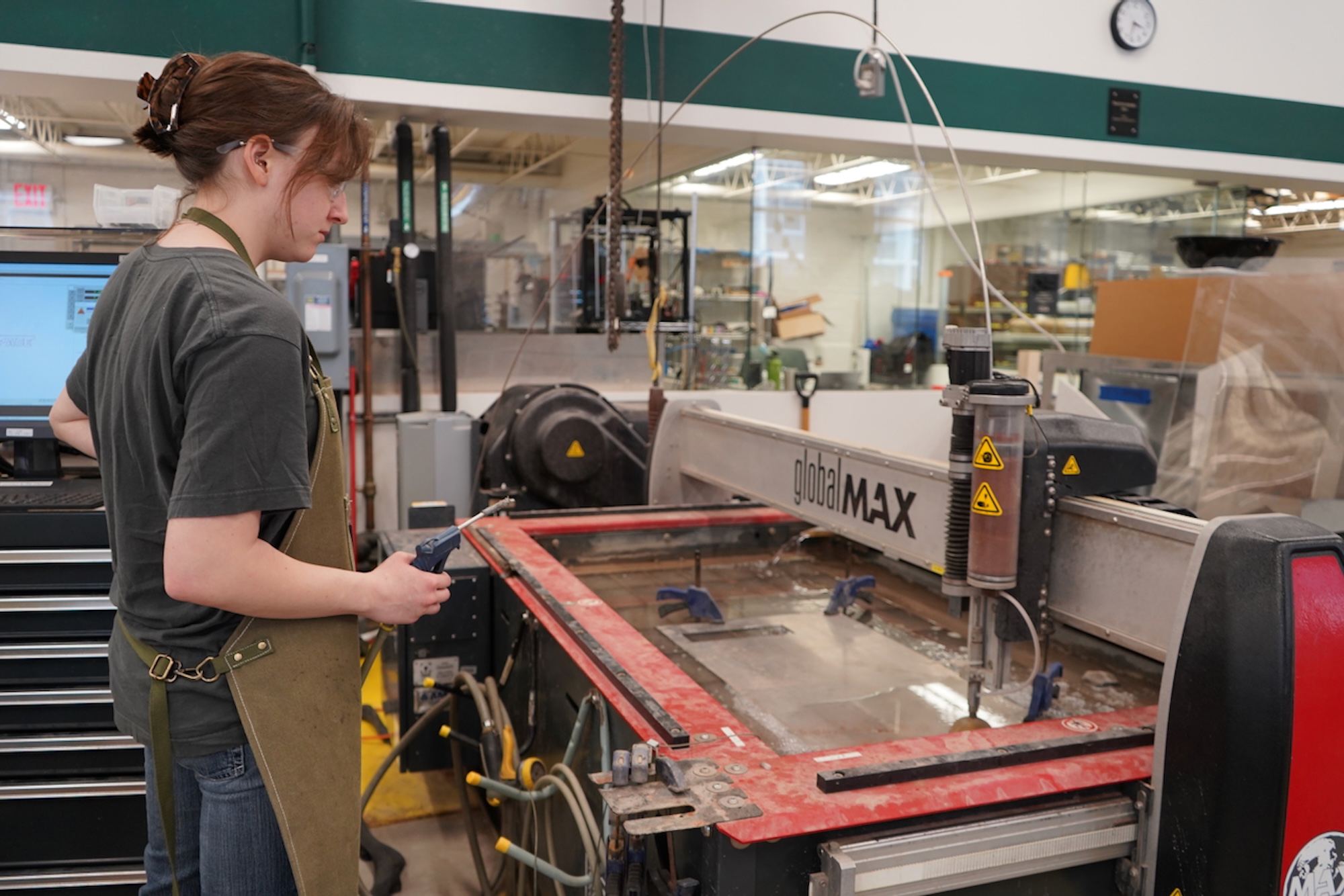 Girl in an apron standing over a laser cutting machine