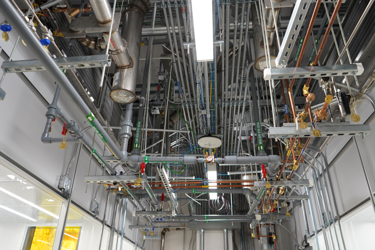 Complex network of pipes, conduits, and lighting fixtures overhead.
