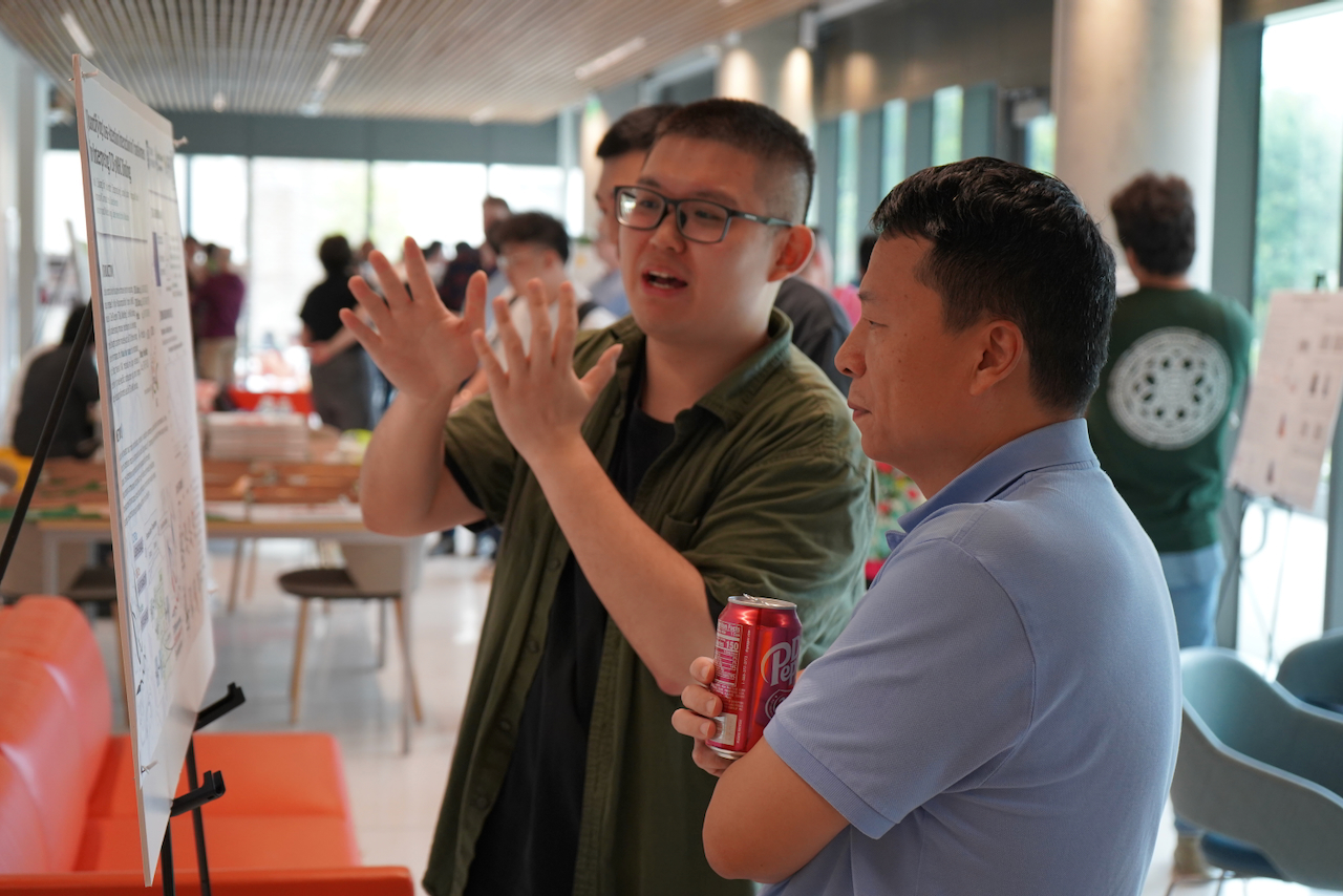 Two men at a poster session, one gesturing while speaking.