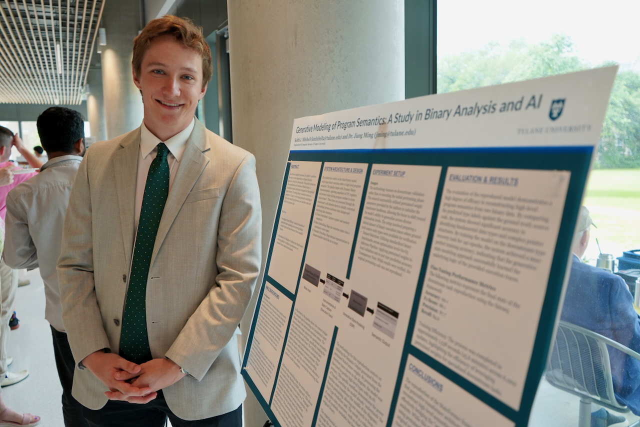 Photograph of a smiling young man in a suit standing next to a research poster.