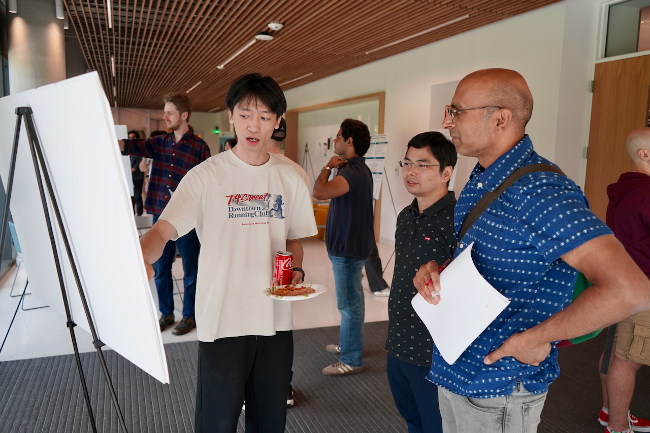 A group of people standing around a poster board, listening to a young man present.