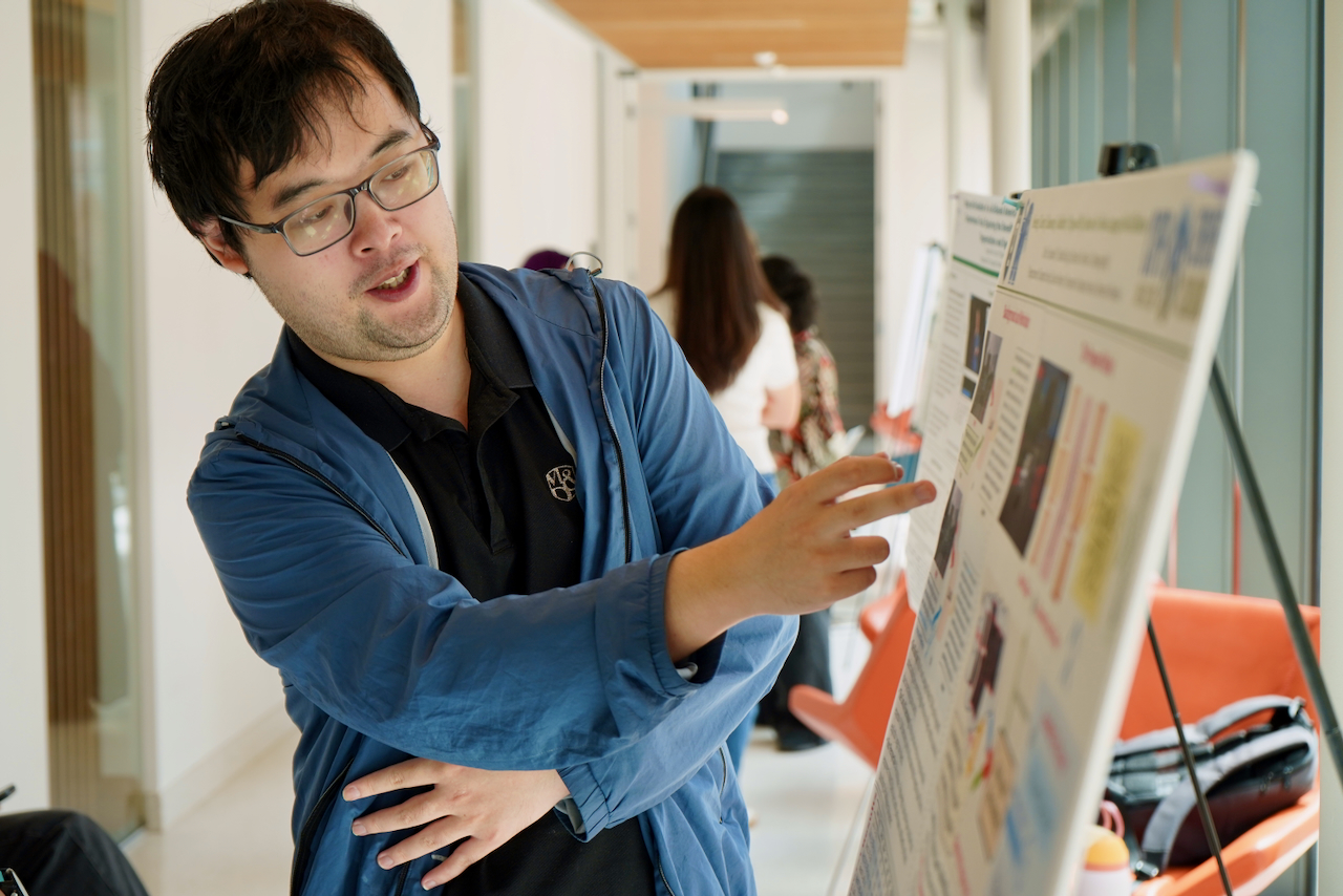 Photograph of a man in a blue jacket pointing at a research poster.