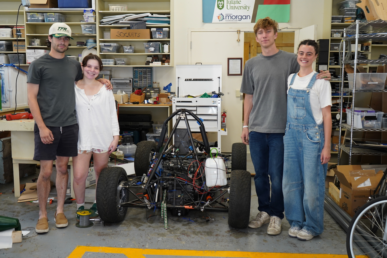 Photo of four students posing with a race car in a workshop.