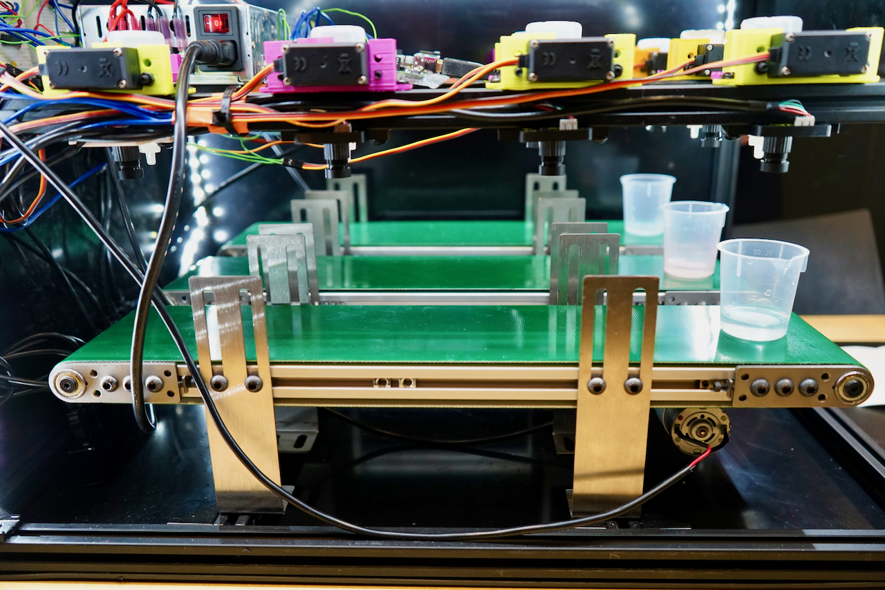Photograph of three green conveyor belts stacked vertically with sensors above.