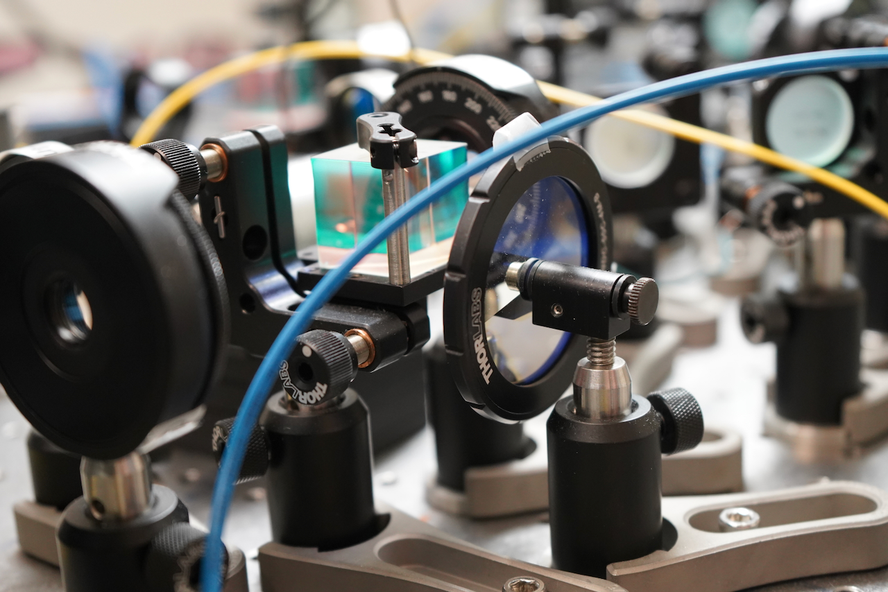 Photograph of an optical table with lenses, mirrors, and fiber optic cables in a lab.