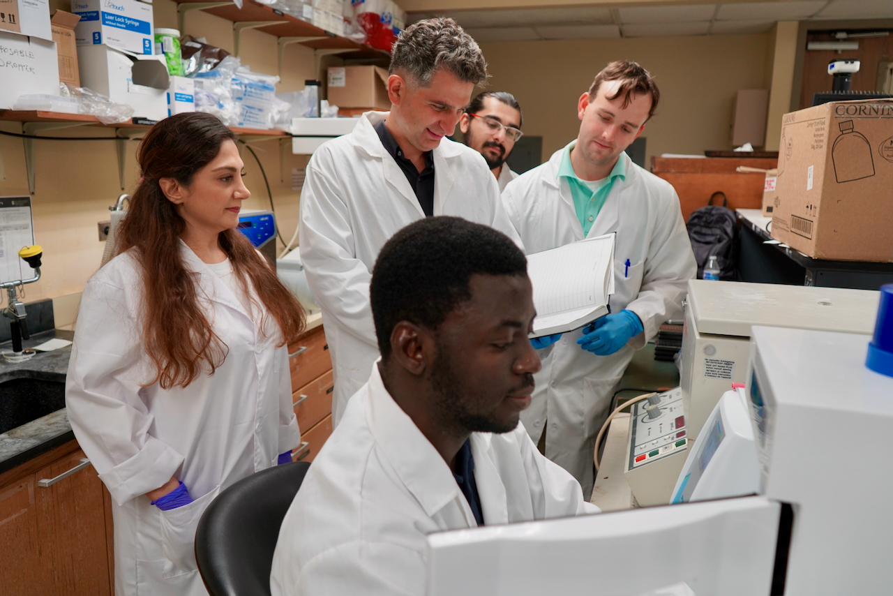 Researchers in lab coats examine a computer screen in a laboratory.