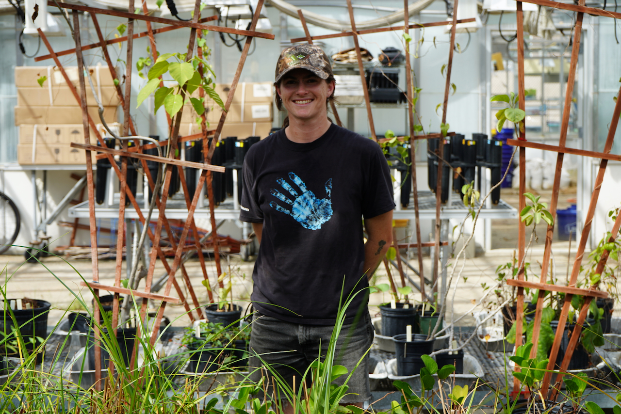 Woman smiling standing in a green house with her hands behind her back