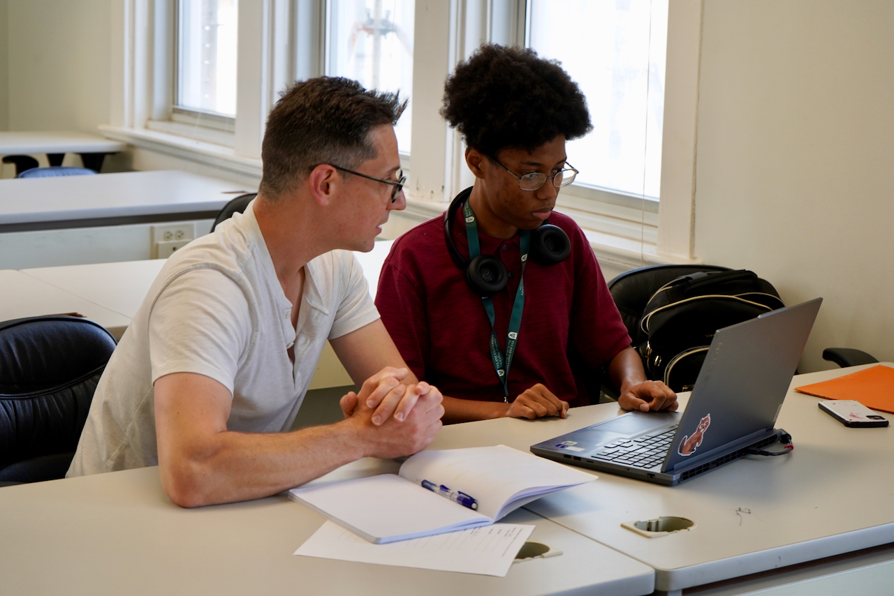 A man and a woman look at a laptop at a desk.