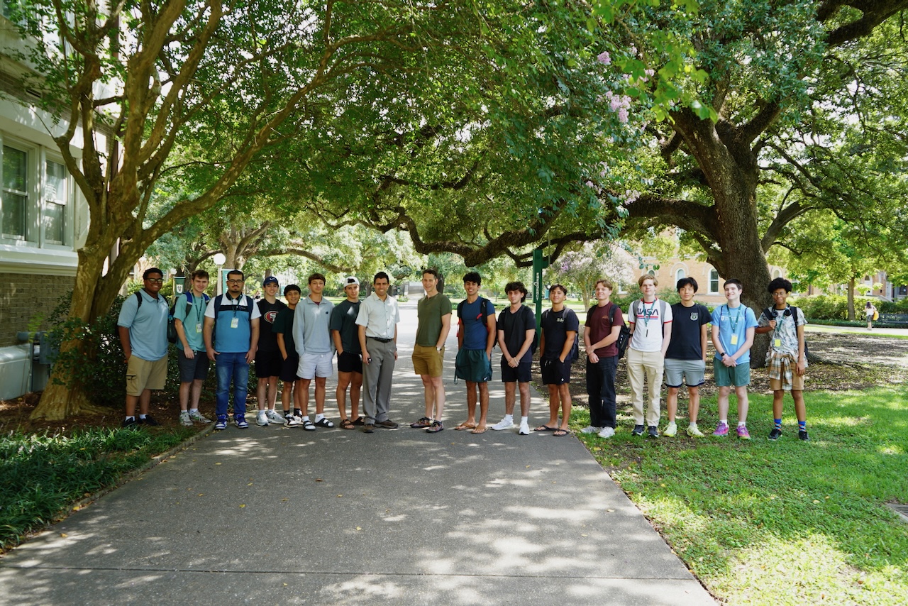 Photograph of a diverse group of seventeen students posing outdoors on a pathway.