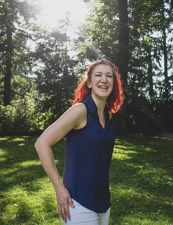 Woman with bright red hair laughing in a sunlit park.