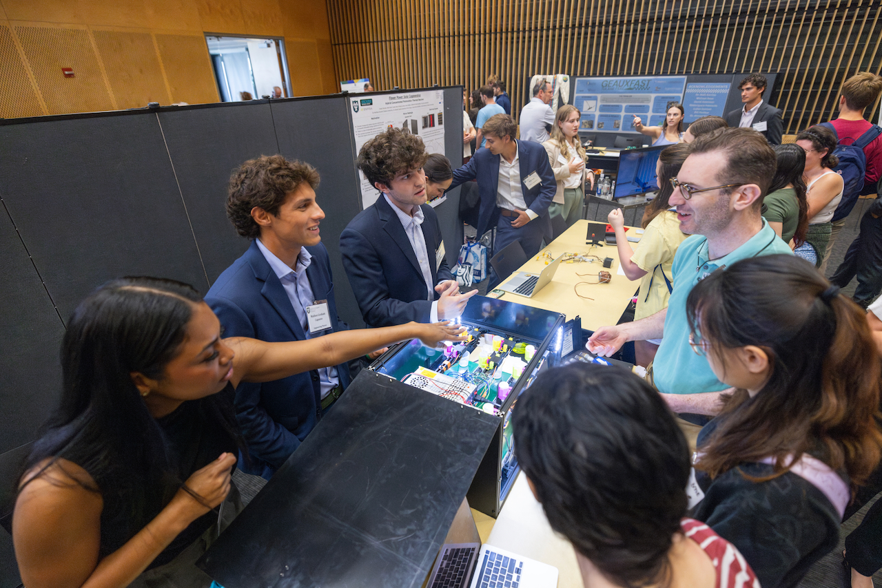 A group of students smiling around a project display in a hall.