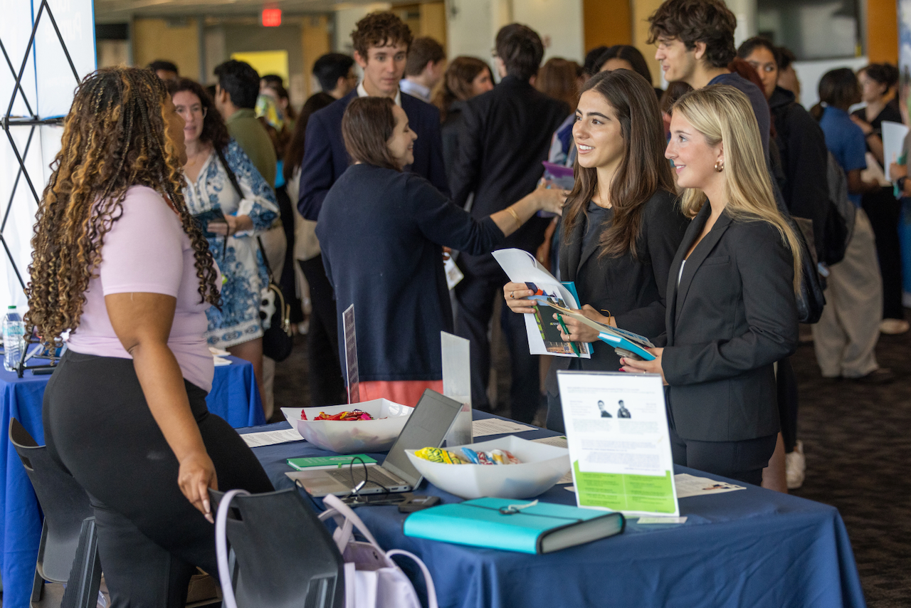 Students at a career fair interact at a table with brochures.