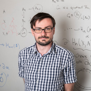 Man in glasses and checkered shirt in front of whiteboard with math equations
