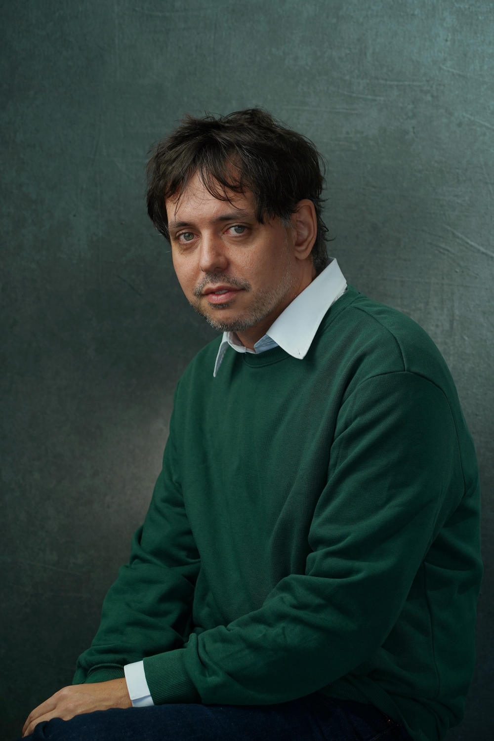 Man in dark green sweater and white collar shirt looking slightly to the left.