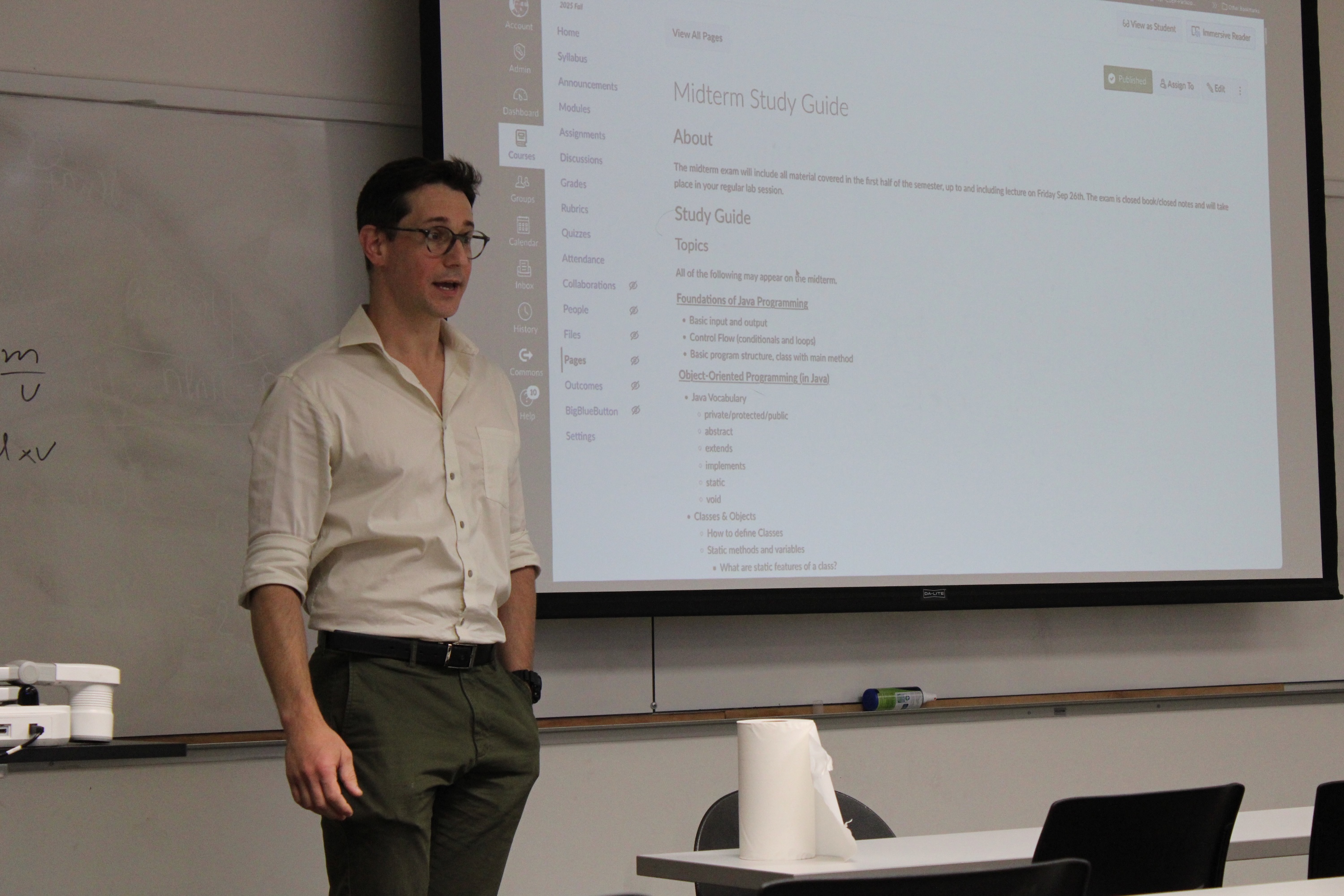 Photograph of a man in a classroom standing in front of a projector screen.