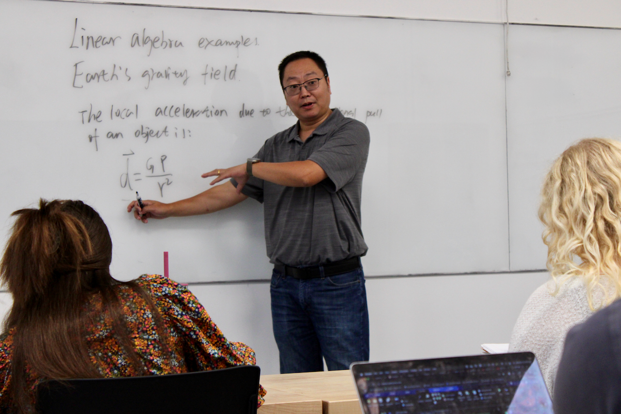 Photograph of a professor teaching in front of a whiteboard to students in a classroom.
