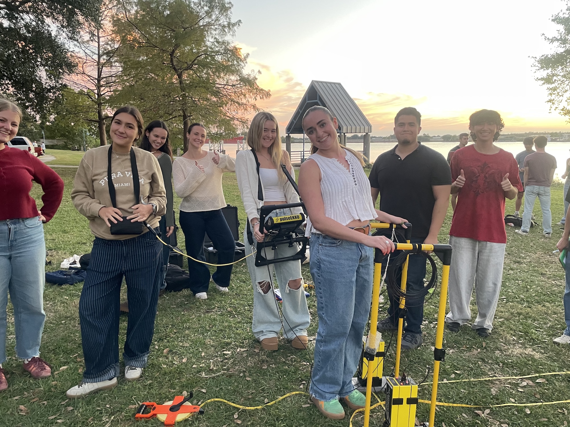 Photo of a group of students standing outdoors near a lake at sunset.