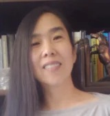 A smiling Asian woman with long dark hair, partially obscured by bookshelves.