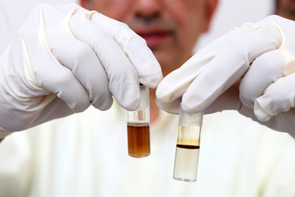 Man wearing white gloves holding two test tubes with liquid in them