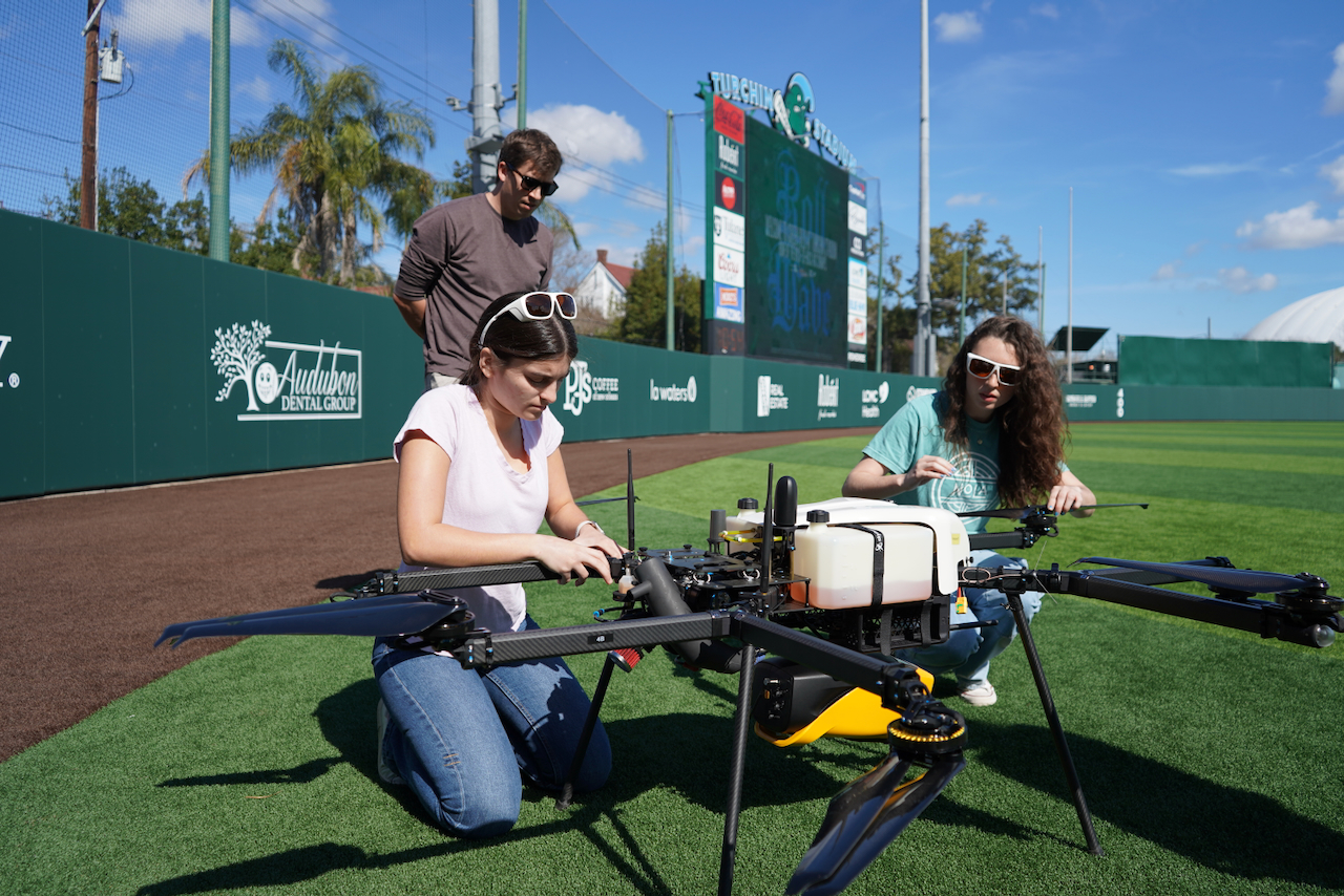 Photo of three people assembling a large agricultural drone on a sports field.