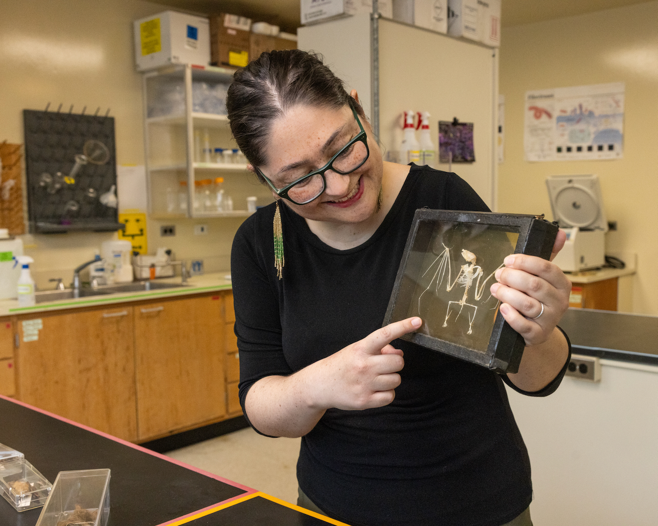 Woman holding a and pointing at a shadow box filled with bone fossils