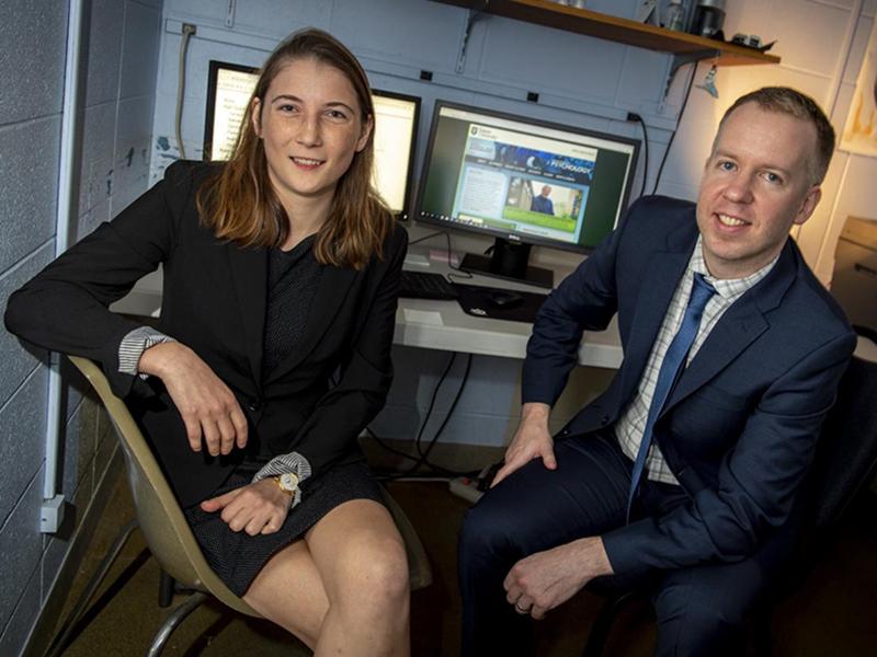 Photograph of two people sitting in office chairs in front of computer monitors.